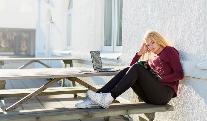 Ung jente sitter på benk og leser.